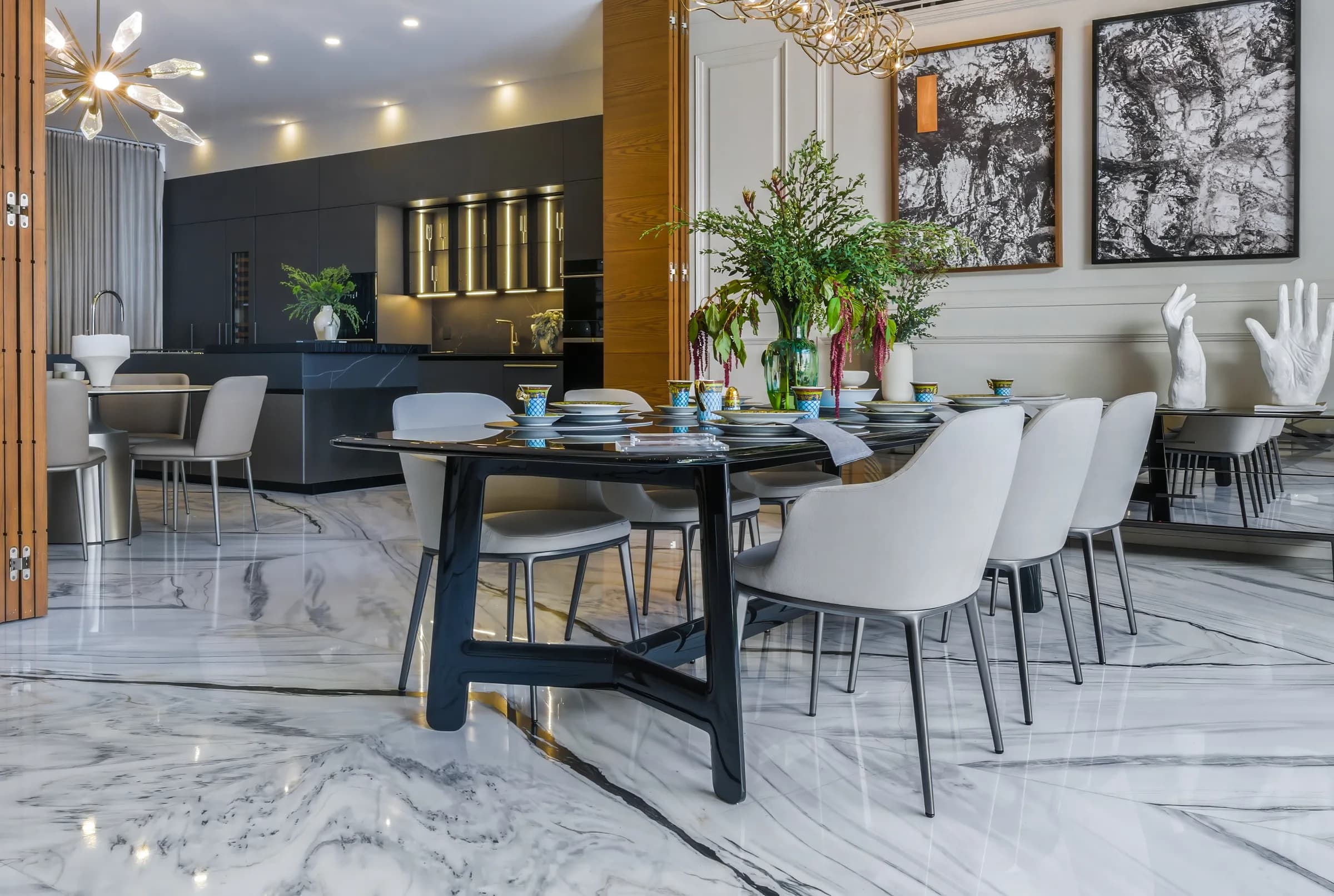 Comedor con mesa negra y sillas claras, con la cocina de gabinetes oscuros al fondo