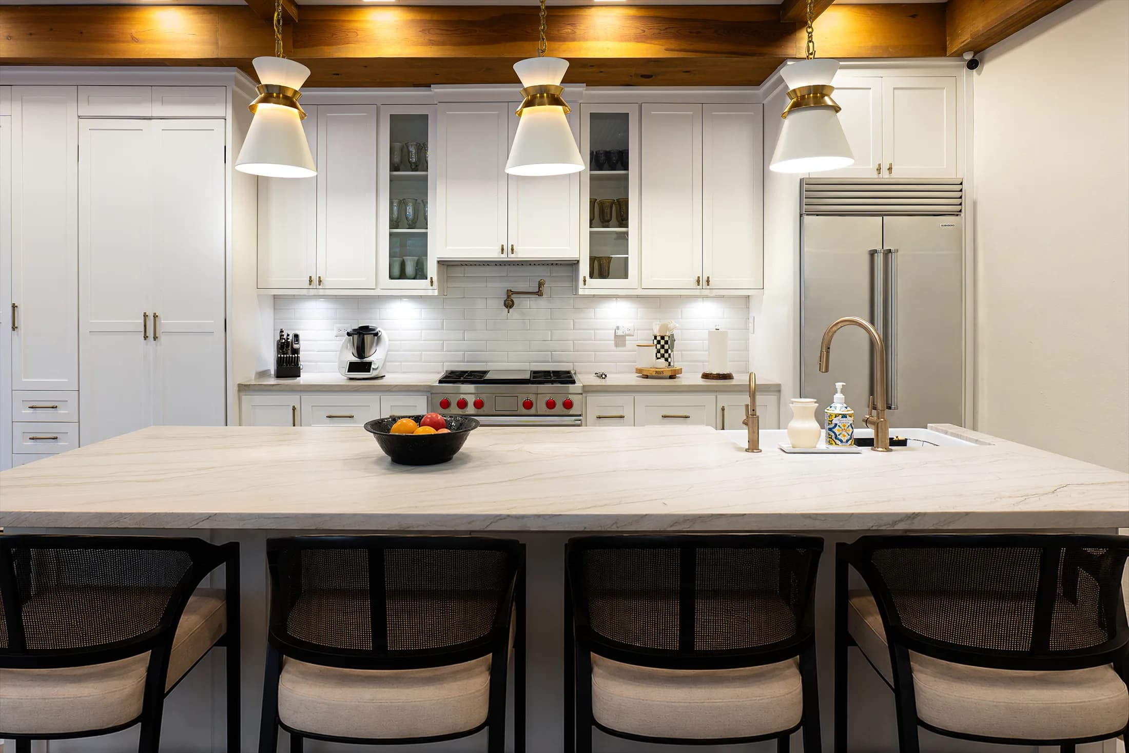 Cocina residencial equipada con parrilla Wolf y refrigerador Sub-Zero, isla de mármol y vigas de madera